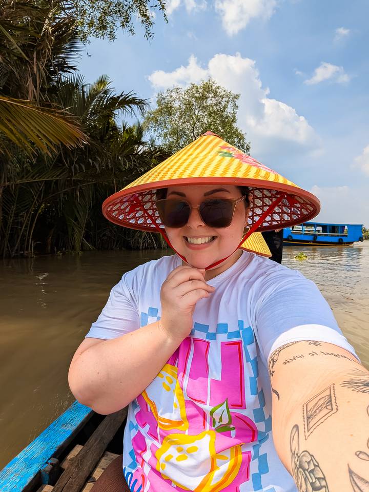 Una persona usando un sombrero tradicional sonriendo a la cámara en un río.
