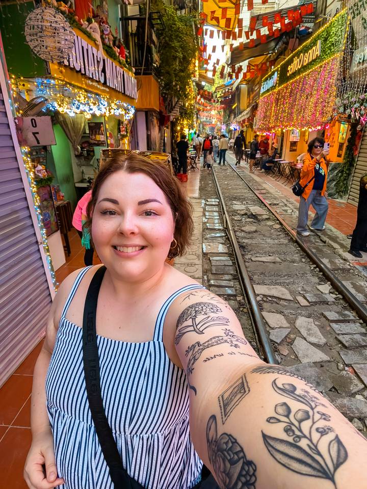 Una persona tomándose una selfie cerca de las vías del tren con gente caminando.