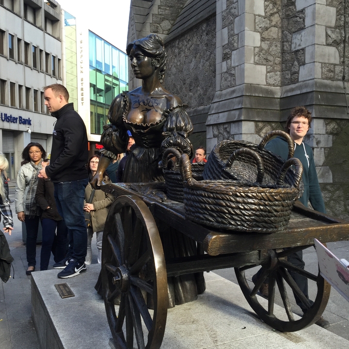 Statue d'une femme avec des paniers observée par des touristes.