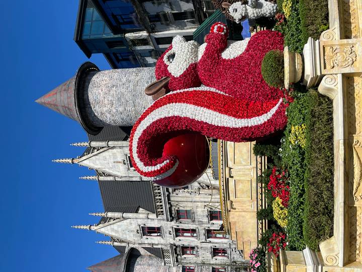 Gran escultura de ardilla hecha de flores frente a una estructura similar a un castillo.