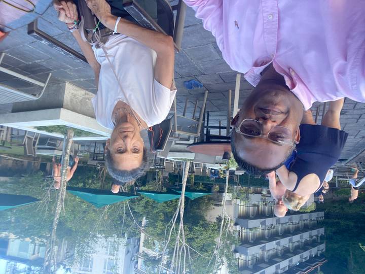 Des gens assis près d'une piscine avec des parasols et un bâtiment en arrière-plan.