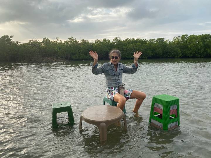 Personne assise sur de petites chaises dans l'eau levant les mains.