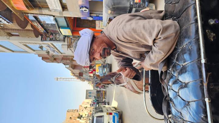 Hombre sentado en un carruaje en una calle concurrida, mostrando el pulgar hacia arriba.