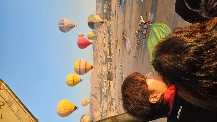 Personas en un globo aerostático mirando otros globos en el cielo.