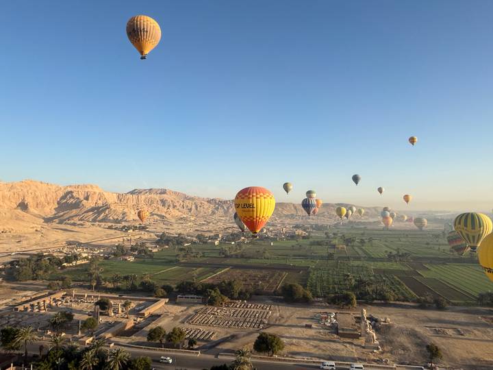Docenas de globos aerostáticos flotando sobre un valle exuberante.
