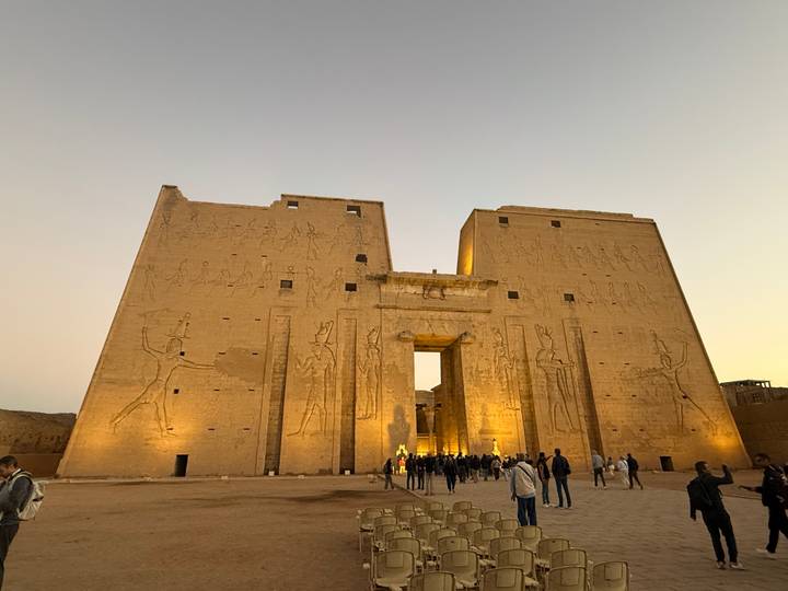 Turistas visitando el antiguo Templo de Edfu durante el atardecer.