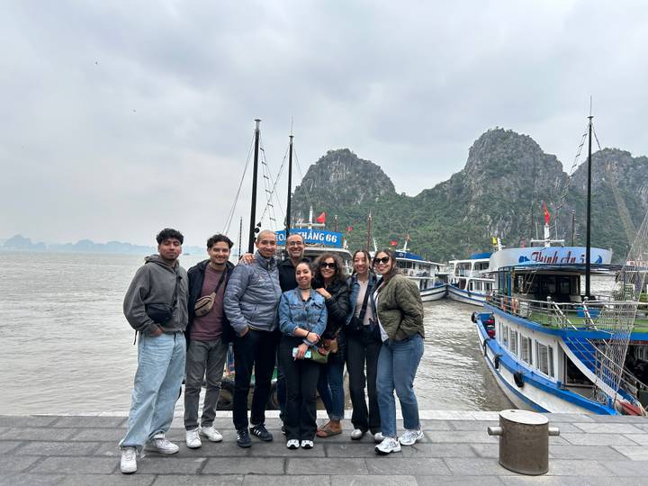 Grupo de personas en un muelle con barcos y formaciones kársticas.