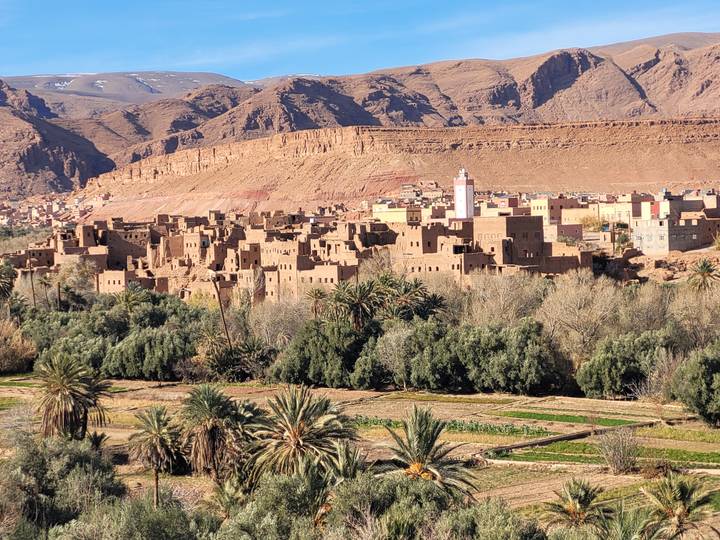 Village marocain traditionnel avec palmiers et montagnes.