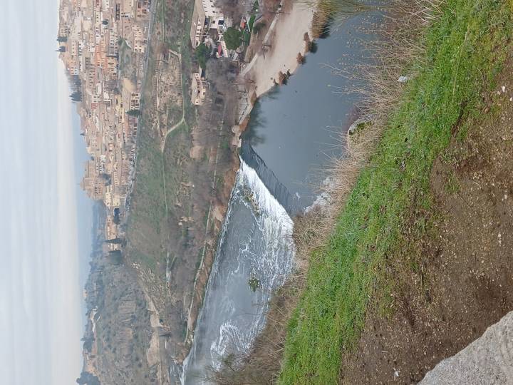 Vista ribereña de la ciudad de Toledo con edificios históricos y una cascada.