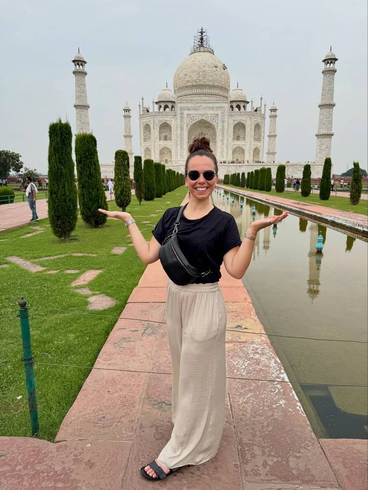 Mujer sonriente posando frente a un famoso monumento histórico con fuentes y árboles.