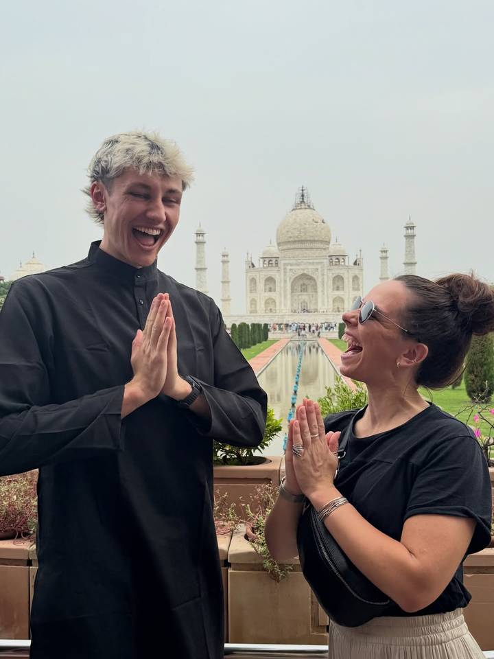 Dúo riendo posando con las manos juntas frente al Taj Mahal.