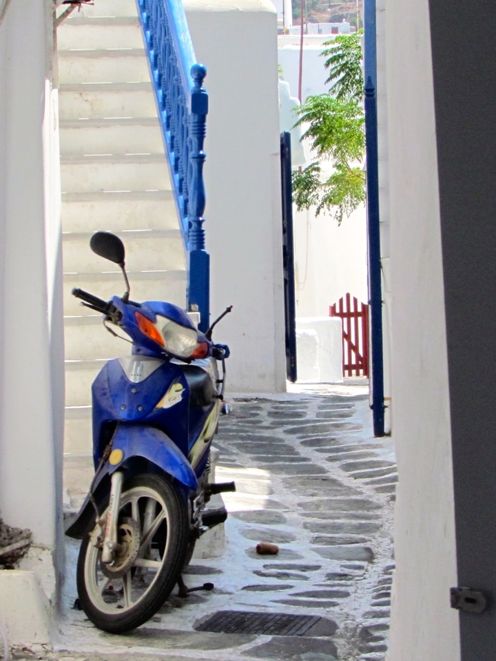 Moto bleue garée dans une rue étroite avec des marches et des portes.