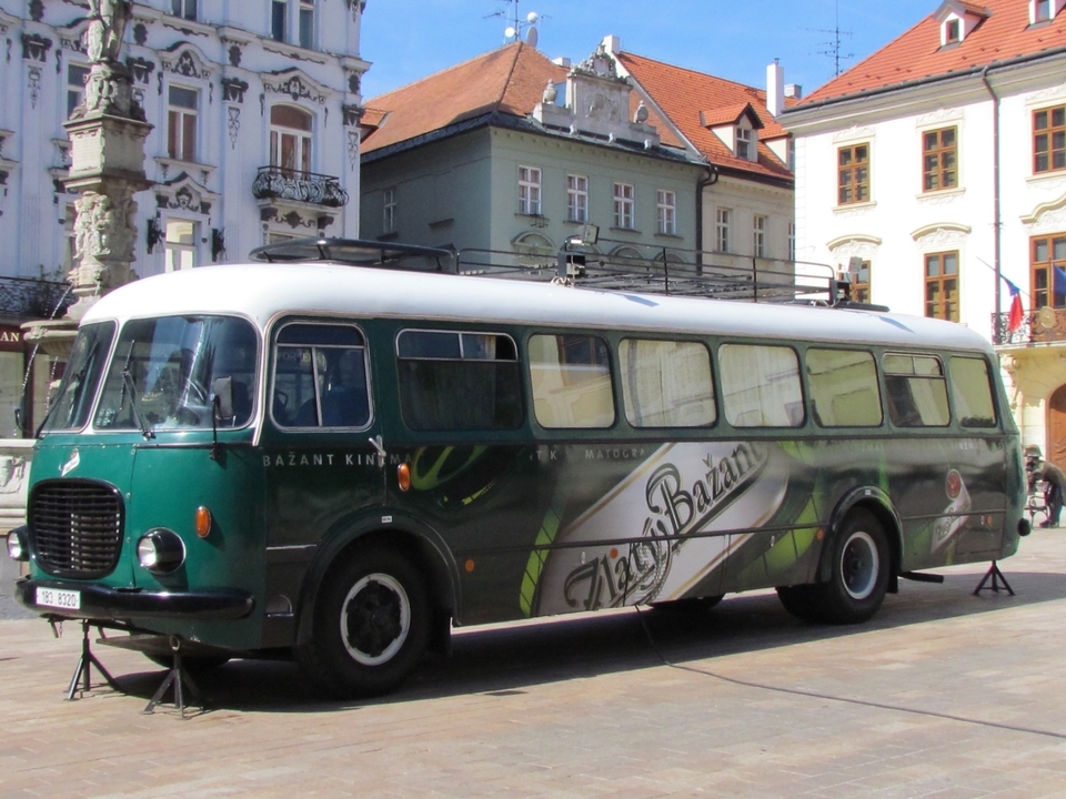 Bus de collection garé sur une place avec des bâtiments anciens.