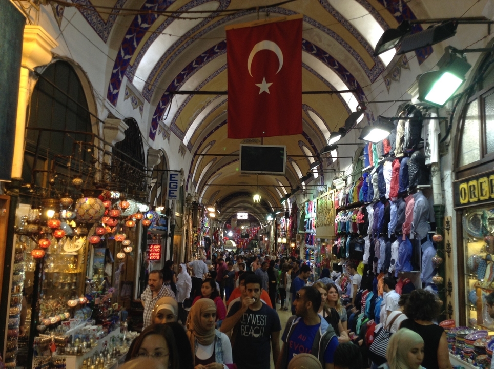 Marché bondé sous une arche avec des drapeaux visibles.