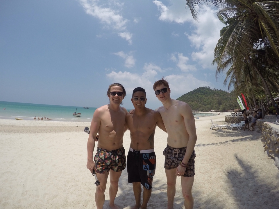 Three friends standing on a beach with the sea in the background.