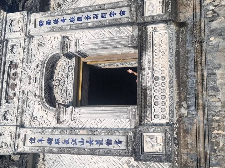 Persona saludando desde la ventana de un edificio de piedra con diseños intrincados.