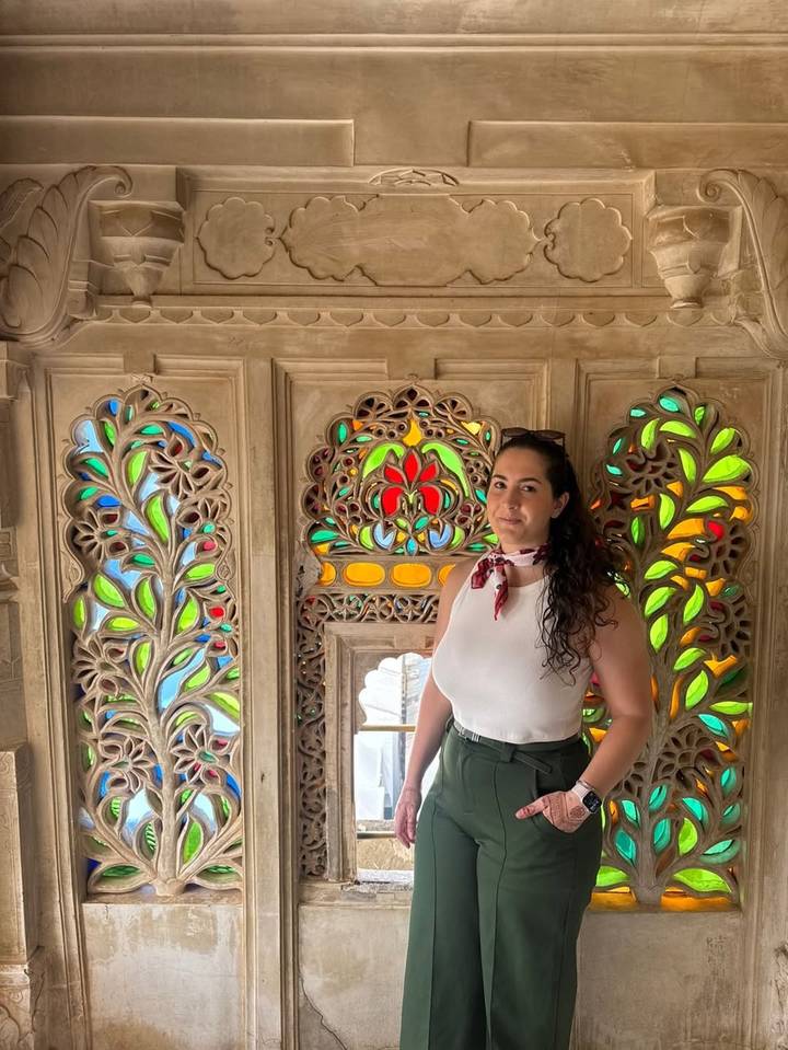 Una mujer posando junto a ventanas de vidrieras en un edificio ornamentado.