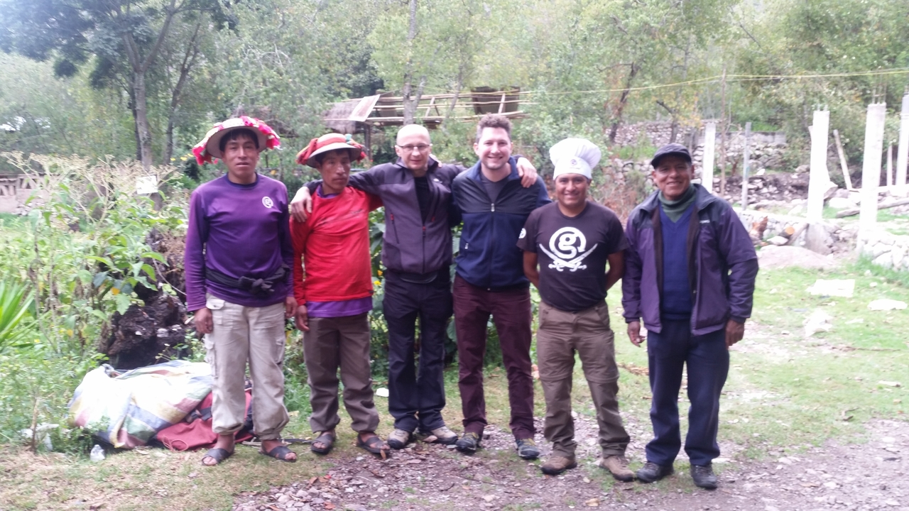Hiking team posing with local cooks and porters in a rural mountain campsite clearing.