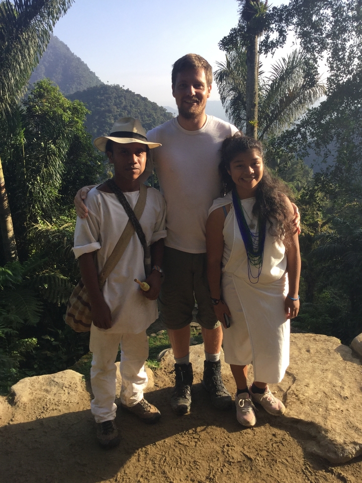 Tourist posing with two indigenous people in traditional white dress amid tropical vegetation