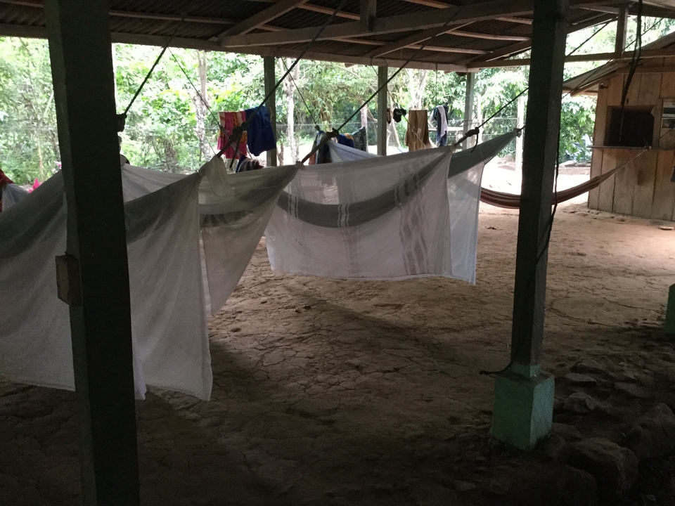 Open-air shelter with dirt floor, hanging hammocks and laundry lines in a jungle camp.