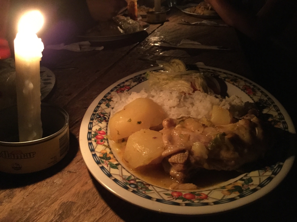 Simple dinner plate of chicken, potatoes and rice lit by a single candle in a dark rustic setting.