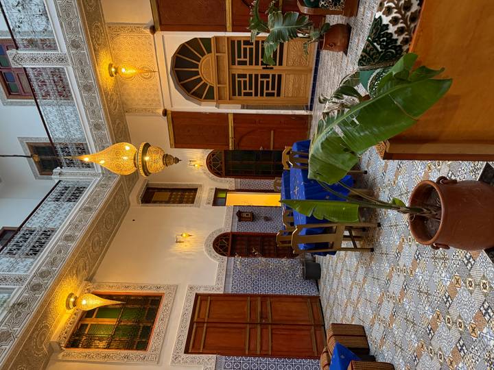 Interior bellamente decorado de un riad con azulejos marroquíes tradicionales e iluminación.