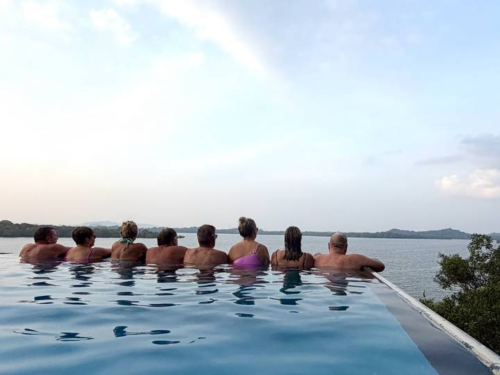 A group of people relaxing in a pool overlooking a serene water landscape.
