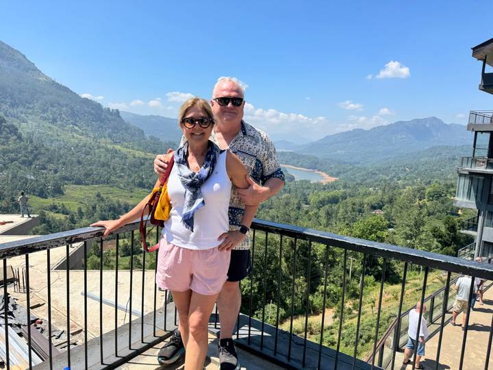 A couple posing with a scenic vista of green mountains and clear skies.