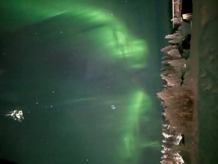 Nordlichter leuchten am Nachthimmel über verschneiter Landschaft mit sichtbaren Sternen.