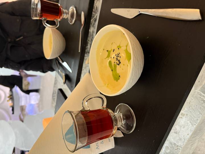 Eine Schüssel cremige Suppe mit einem roten Getränk auf einem schwarzen Tablett.