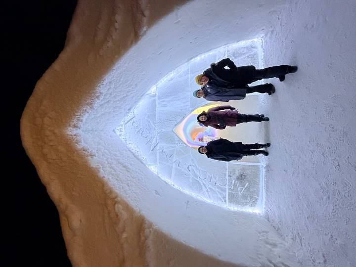 Gruppe von vier Personen, die nachts unter einem leuchtenden Eisbogen-Eingang stehen.