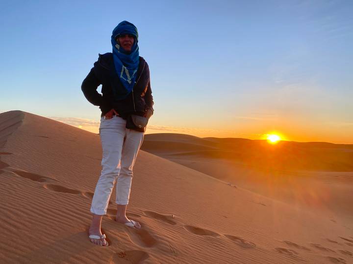 Person auf einer Sanddüne bei Sonnenuntergang mit der tief stehenden Sonne am Himmel.