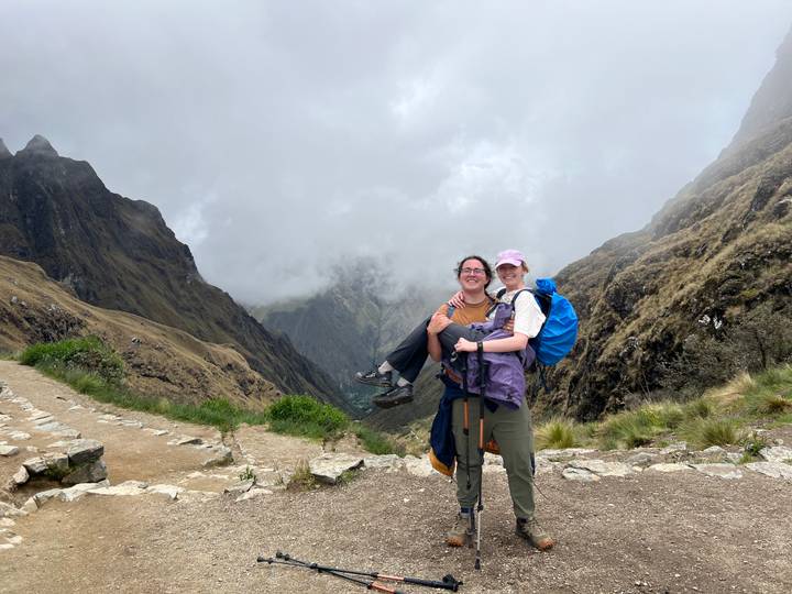 Zwei Personen posieren auf einem Bergpfad mit bewölktem Hintergrund.