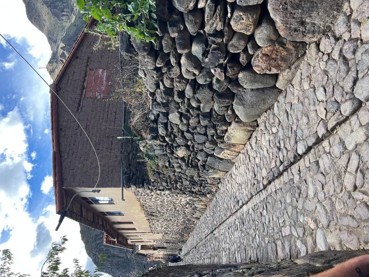 Kopfsteinpflasterstraße mit Lehmziegelhaus und Steinmauer.