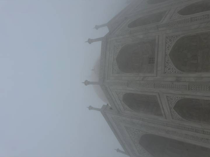 Taj Mahal shrouded in thick morning fog, its marble silhouette barely visible.