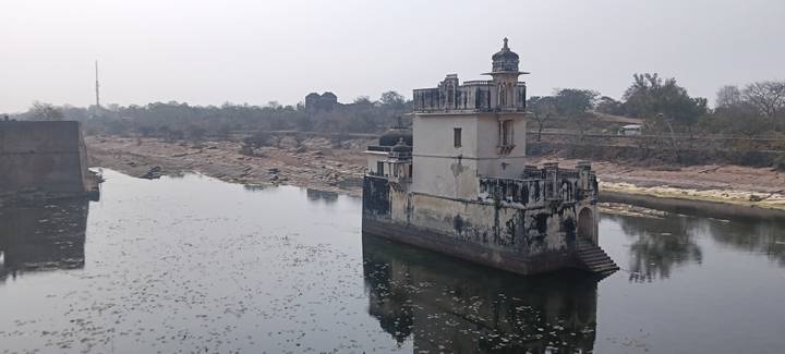 An ancient structure on a lake with surrounding trees and calm waters.
