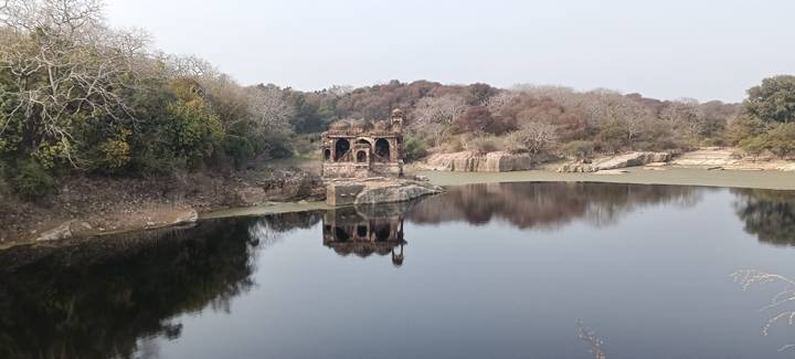 A small ancient building with surrounding trees and reflections in a lake.