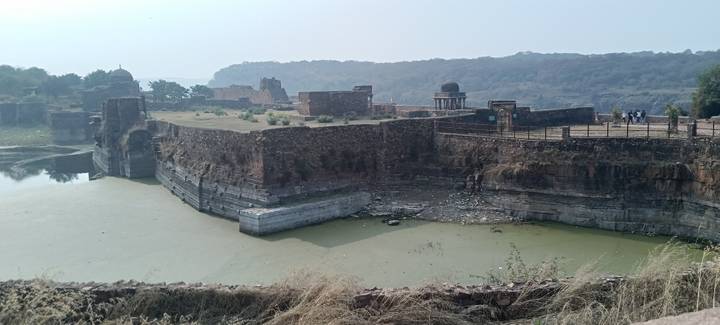 Old fort ruins by water with distant trees and a cloudy sky.