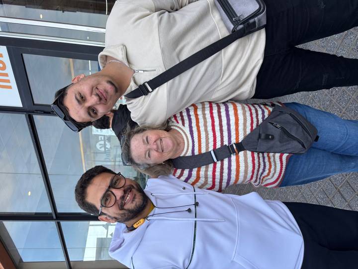 Three people posing in front of a modern building entrance.