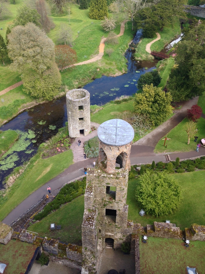Drone view over Blarney Castle grounds showing round towers, moat and lush gardens