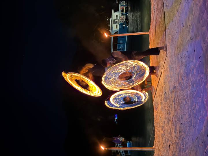 Beach fire performers spinning blazing rings of flame against the dark sea at night.