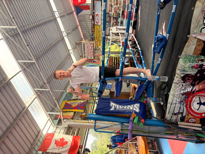 Young traveller posing confidently in a Muay Thai boxing ring inside a flag-decorated open-air gym.