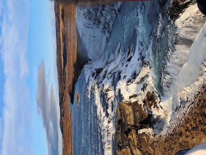 Powerful multi-tiered Gullfoss waterfall cascades through icy canyon under blue winter sky.