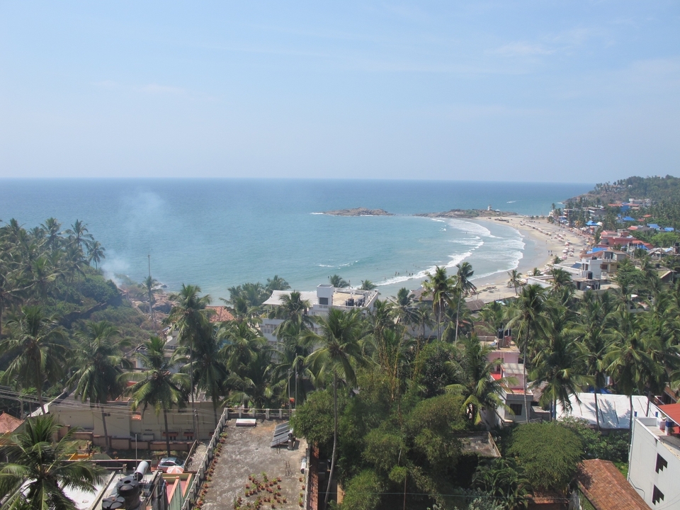 Bord de mer avec des palmiers et un phare au loin.