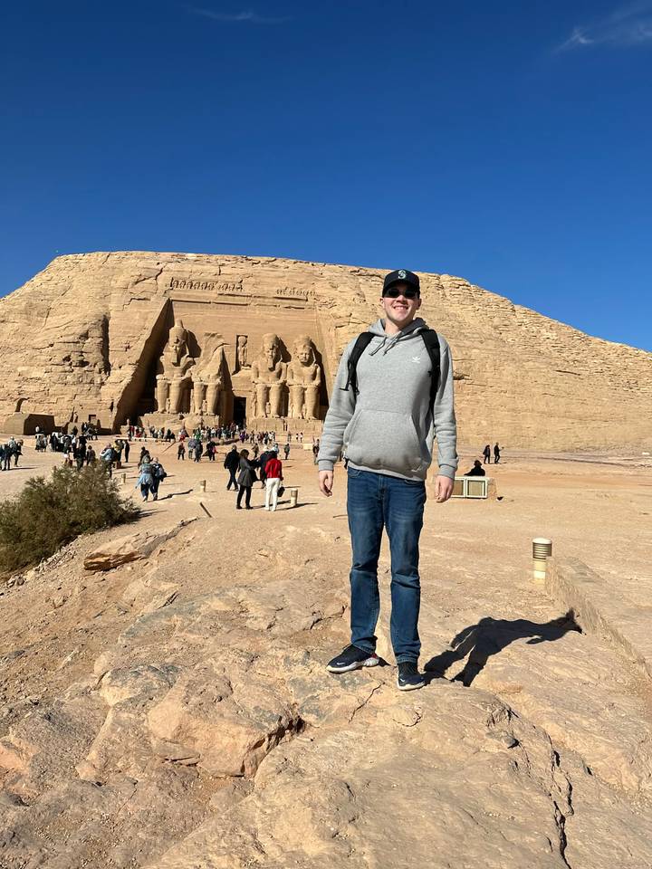 Traveler smiling in front of the monumental statues of Abu Simbel in the desert