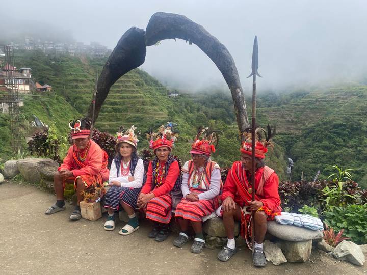 Group of indigenous elders in traditional attire seated before misty rice terraces