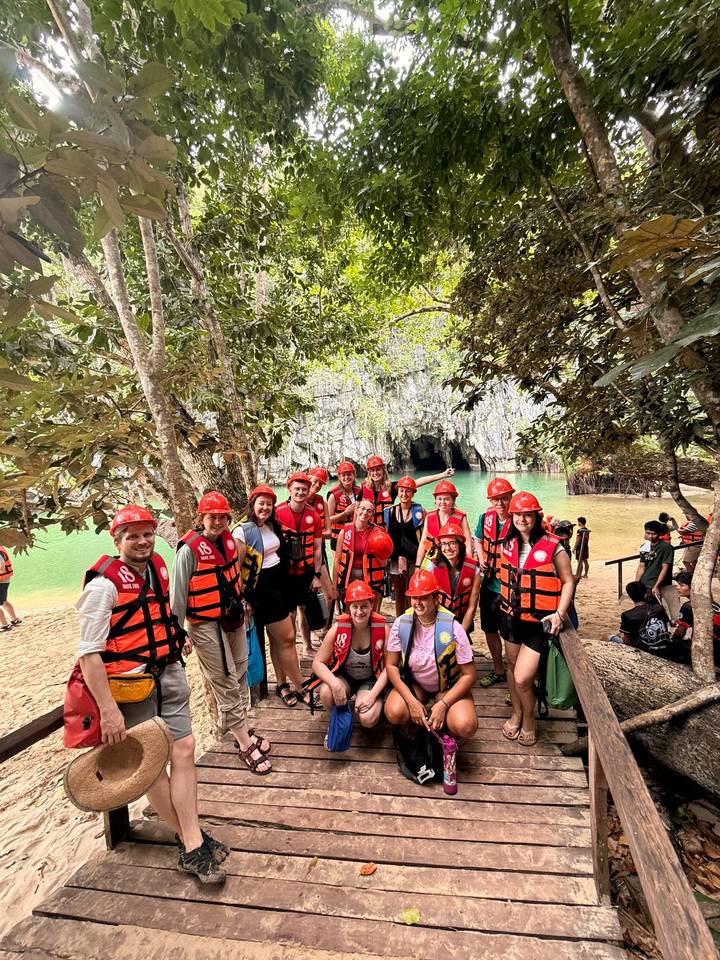 Tour group in life vests and helmets pose before Puerto Princesa Underground River entrance.