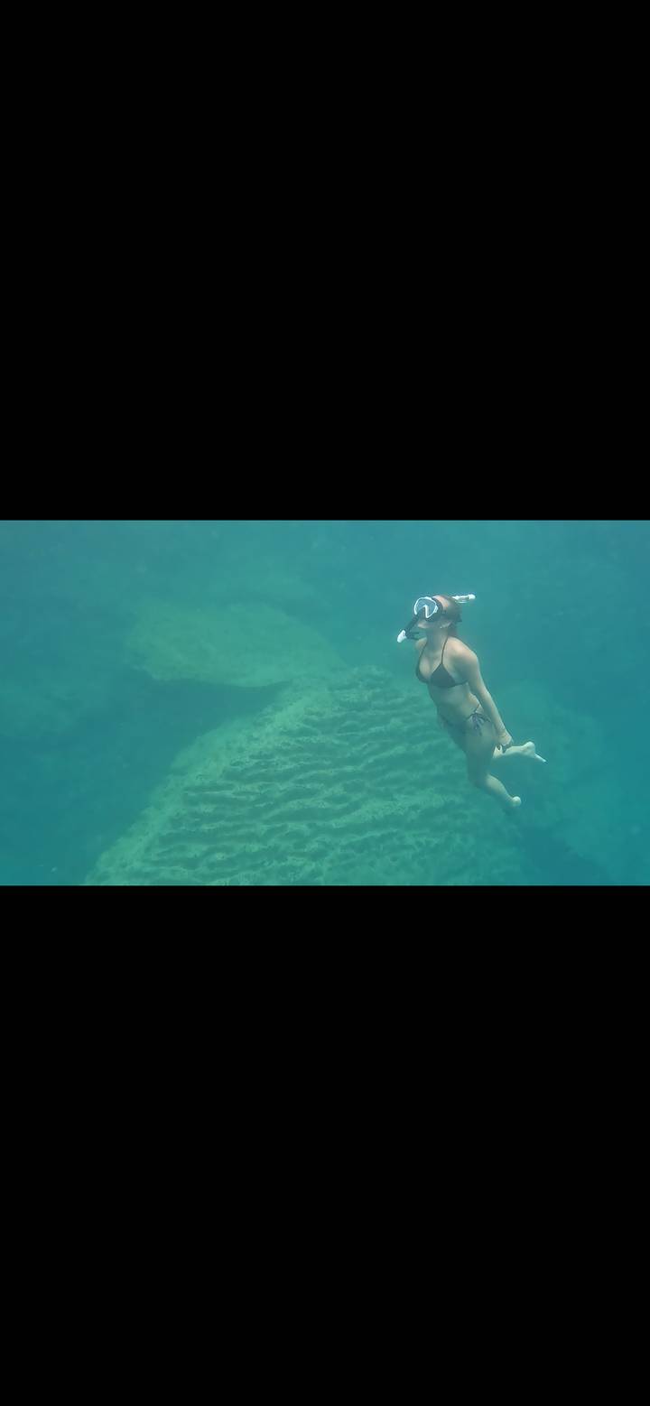 Underwater shot of snorkeler gliding above coral rock in clear blue sea.