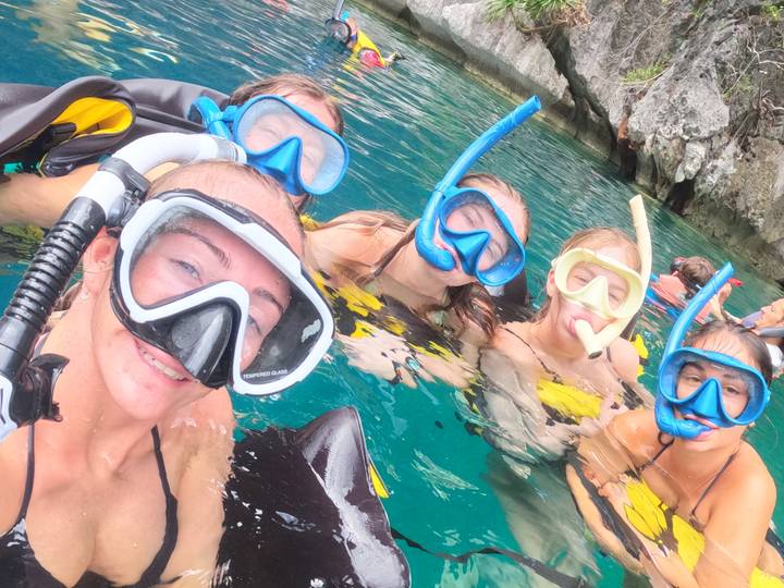 Group selfie of snorkelers wearing masks floating in clear turquoise water.