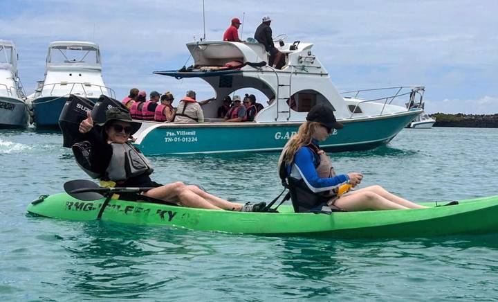 Two travelers paddling a tandem green kayak in a marina with tour boats nearby.